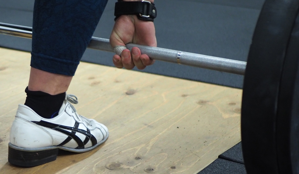 A hand gripping a barbell, with a weightlifting shoe.